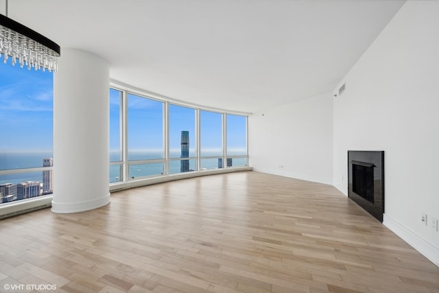 unfurnished living room featuring light hardwood / wood-style flooring, a water view, and a wall of windows