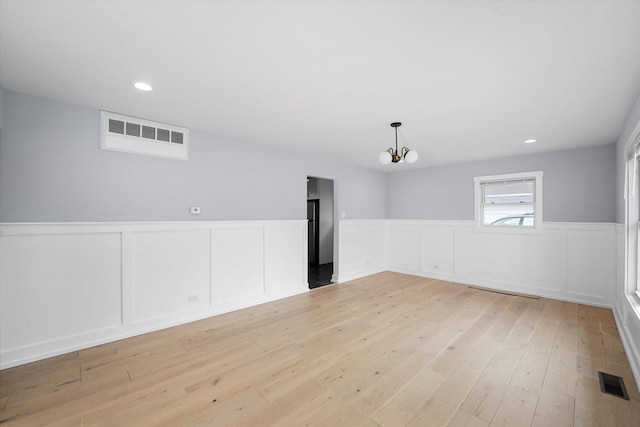 unfurnished room with a wainscoted wall, visible vents, light wood-style flooring, and an inviting chandelier