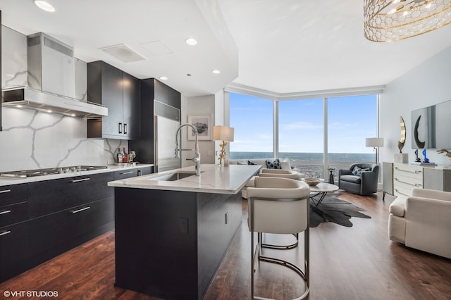 kitchen featuring wall chimney range hood, dark hardwood / wood-style floors, expansive windows, sink, and a breakfast bar