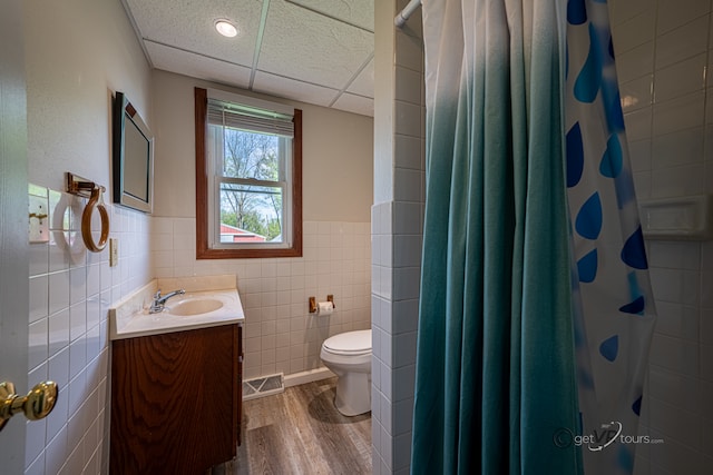 bathroom with tile walls, toilet, vanity, hardwood / wood-style floors, and a paneled ceiling