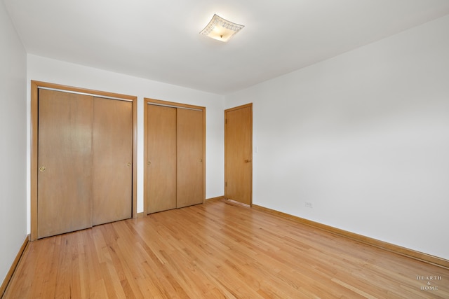 unfurnished bedroom featuring light hardwood / wood-style floors and two closets