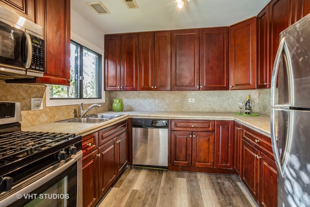 kitchen with backsplash, stainless steel appliances, light wood-type flooring, and sink