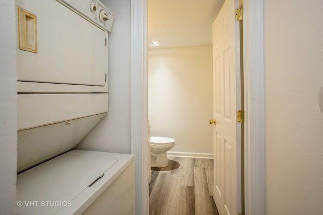 bathroom with wood-type flooring, stacked washer / dryer, and toilet