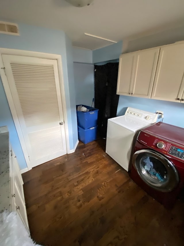 clothes washing area featuring washer and clothes dryer, dark wood-type flooring, and cabinets