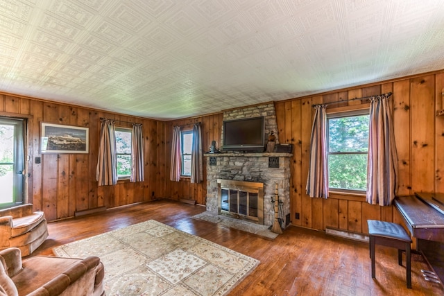 living room with a wealth of natural light, a stone fireplace, wooden walls, and hardwood / wood-style flooring