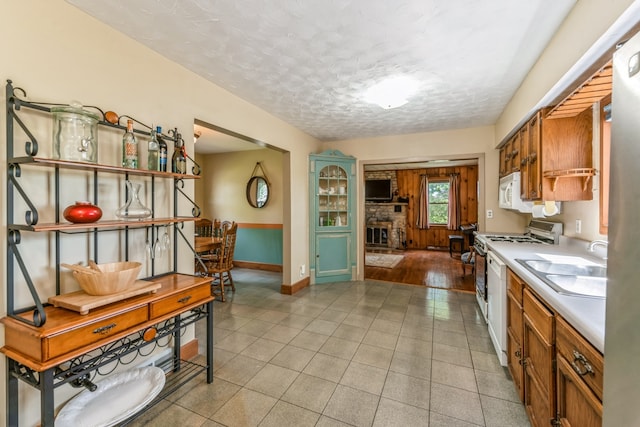 kitchen with light hardwood / wood-style flooring, white appliances, a fireplace, a textured ceiling, and sink