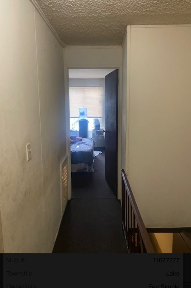 hallway featuring dark carpet and a textured ceiling