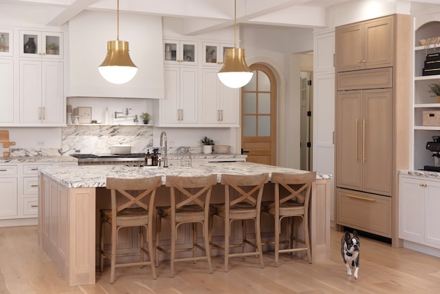 kitchen featuring light stone counters, pendant lighting, light hardwood / wood-style floors, and a kitchen island with sink