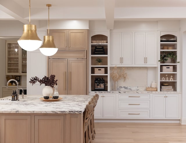 kitchen with paneled built in fridge, light hardwood / wood-style flooring, a center island with sink, pendant lighting, and light stone countertops