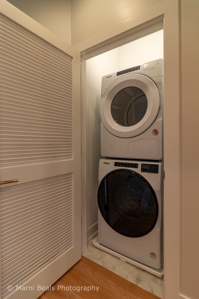 clothes washing area featuring stacked washer and clothes dryer and hardwood / wood-style flooring