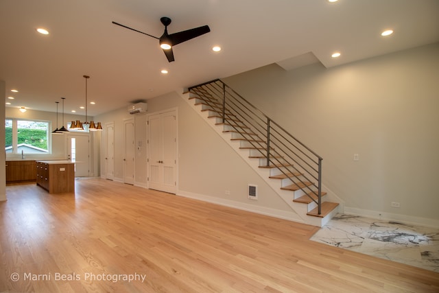 unfurnished living room with light hardwood / wood-style floors, ceiling fan, and a wall mounted air conditioner