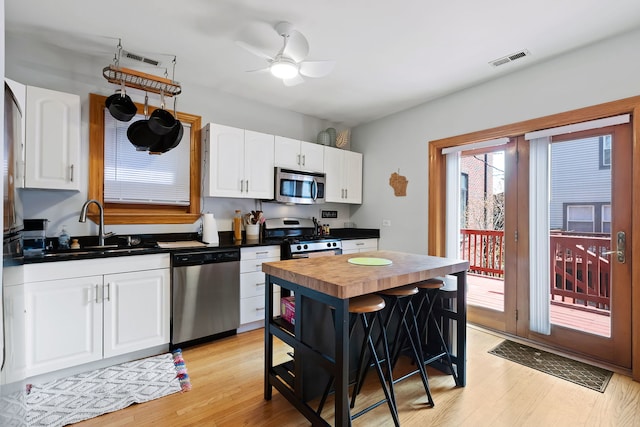 kitchen featuring white cabinetry, stainless steel appliances, a kitchen island, light hardwood / wood-style floors, and ceiling fan