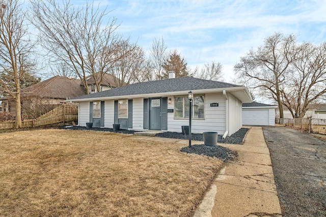 single story home featuring a garage, a shingled roof, fence, an outdoor structure, and a front yard