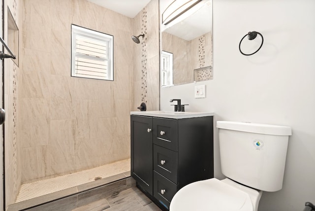 bathroom with vanity with extensive cabinet space, a tile shower, and toilet