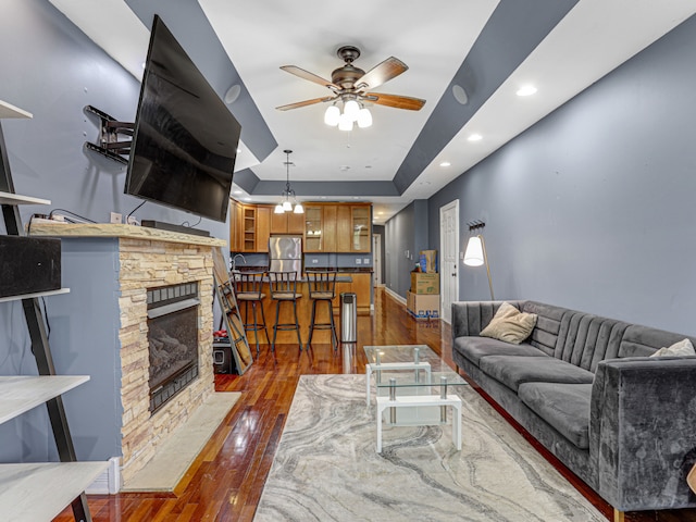 living room featuring a stone fireplace, ceiling fan, dark hardwood / wood-style floors, and a tray ceiling