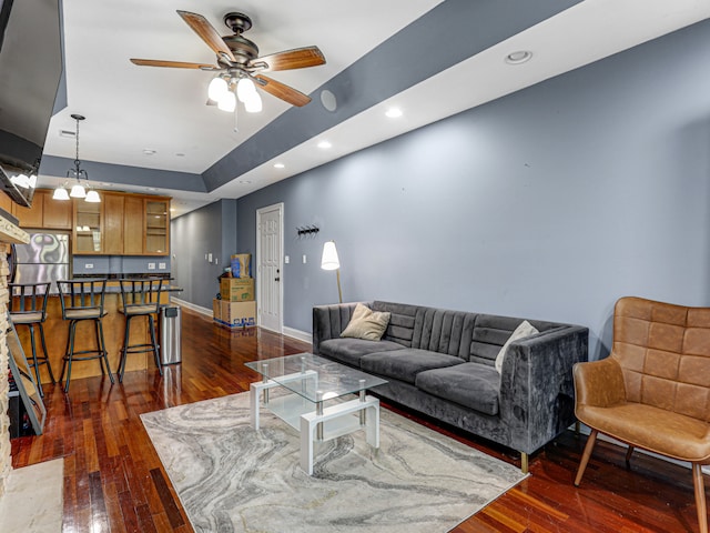 living room with ceiling fan, a raised ceiling, and dark wood-type flooring