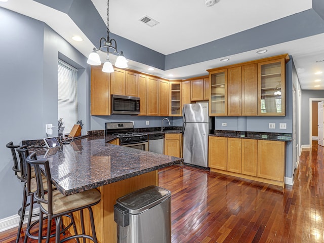 kitchen with a kitchen bar, hanging light fixtures, stainless steel appliances, and dark wood-type flooring