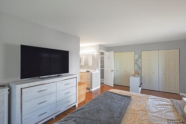 bedroom with two closets, wood finished floors, and ensuite bathroom
