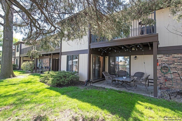 rear view of property featuring brick siding, a patio area, a balcony, and a yard