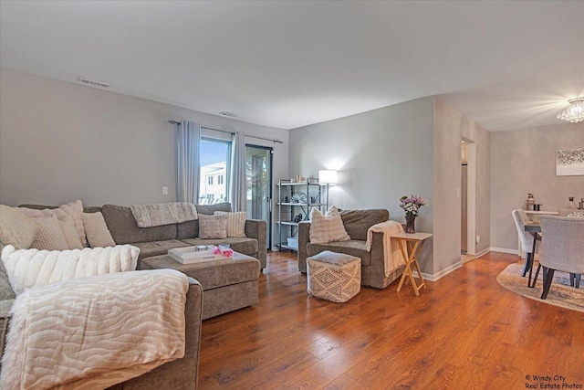 living area featuring baseboards, a chandelier, wood finished floors, and visible vents