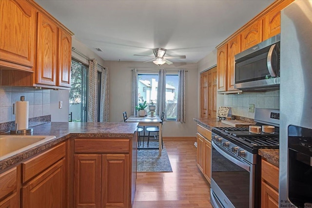 kitchen featuring decorative backsplash, a peninsula, a ceiling fan, light wood finished floors, and appliances with stainless steel finishes
