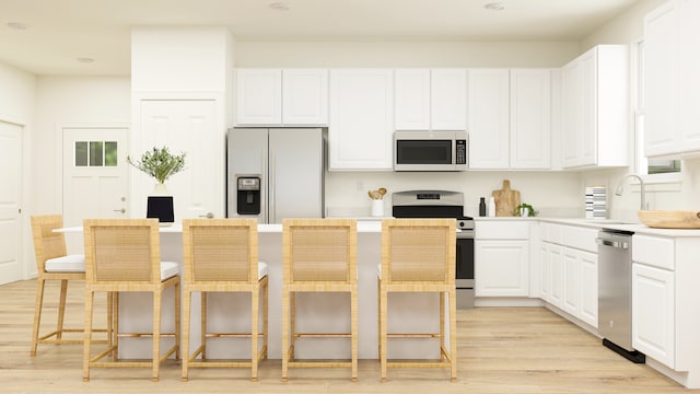 kitchen featuring white cabinets, light hardwood / wood-style floors, appliances with stainless steel finishes, and a kitchen breakfast bar