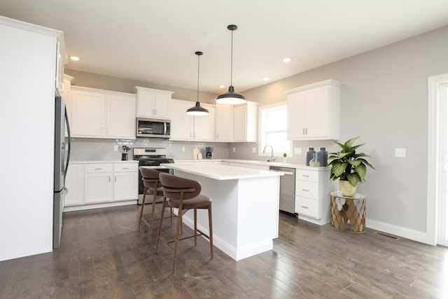 kitchen with decorative light fixtures, dark hardwood / wood-style flooring, a kitchen bar, a center island, and appliances with stainless steel finishes