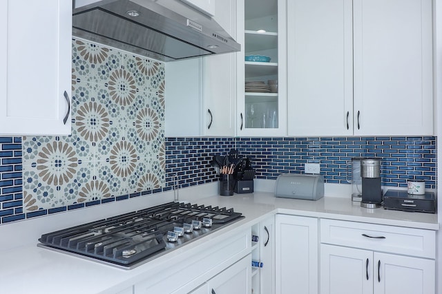 kitchen with light countertops, stainless steel gas stovetop, white cabinets, glass insert cabinets, and exhaust hood