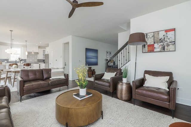 living room with stairs, wood finished floors, baseboards, and ceiling fan