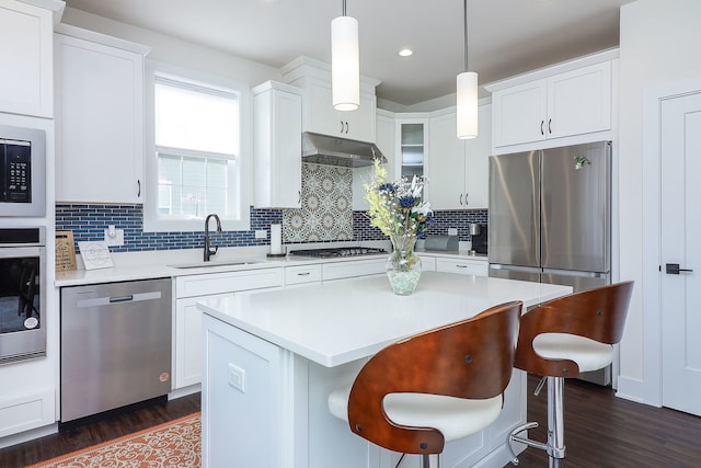 kitchen with a breakfast bar area, a sink, stainless steel appliances, light countertops, and under cabinet range hood