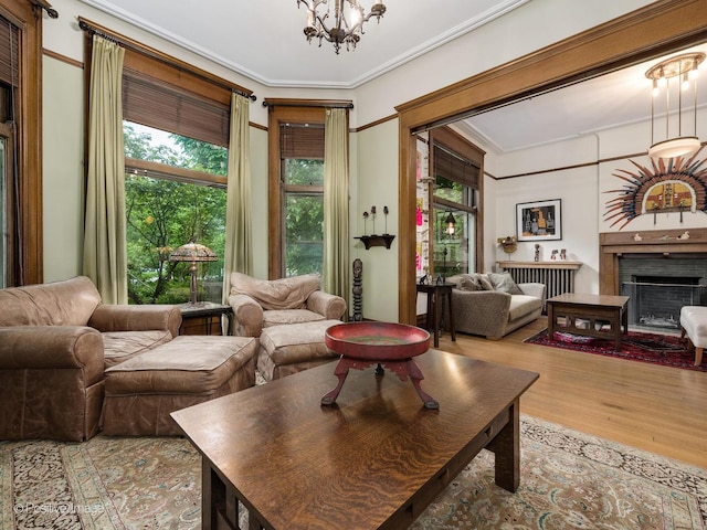 living area featuring a chandelier, a fireplace, wood finished floors, and crown molding