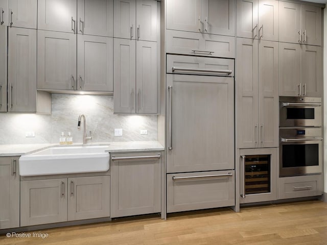 kitchen with beverage cooler, a sink, backsplash, paneled appliances, and light wood finished floors