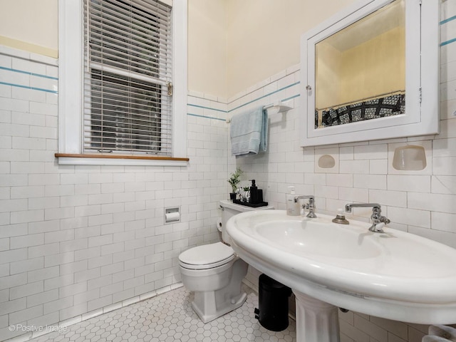 half bath featuring toilet, tile patterned flooring, tile walls, and a sink