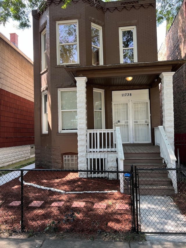 view of front of property with a fenced front yard, covered porch, brick siding, and a gate