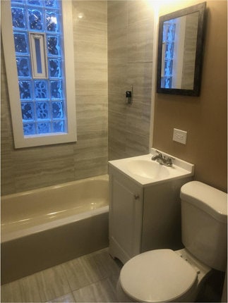 full bathroom with tiled shower / bath combo, vanity, toilet, and tile patterned flooring