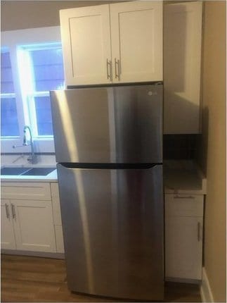 kitchen with wood finished floors, a sink, white cabinets, light countertops, and freestanding refrigerator