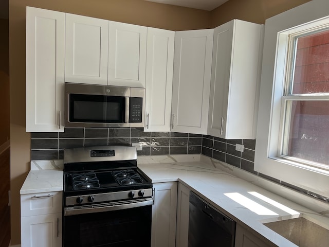 kitchen featuring appliances with stainless steel finishes, white cabinetry, light stone counters, and backsplash