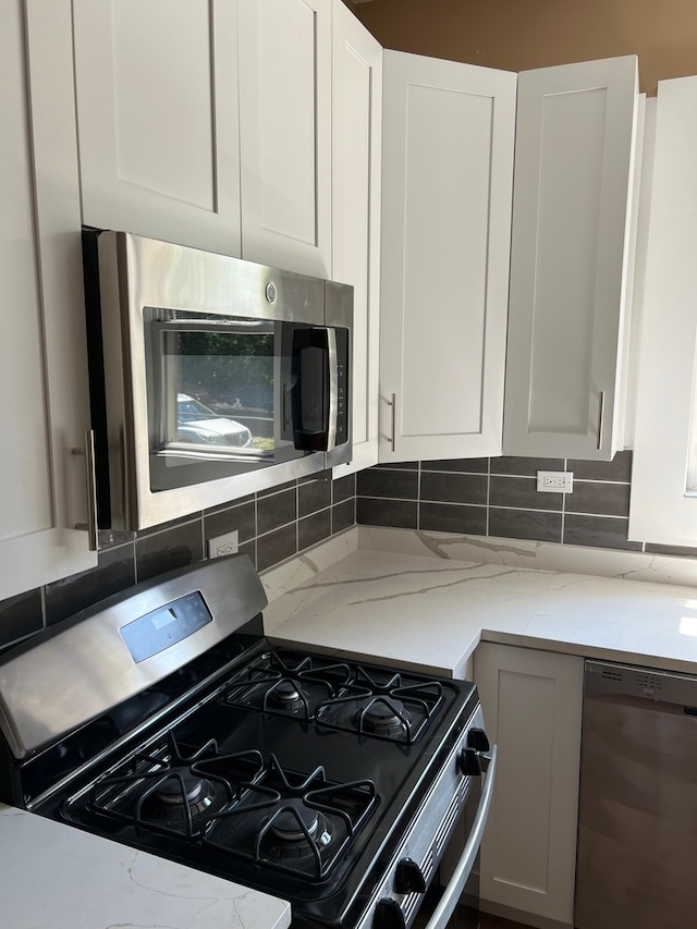 kitchen featuring appliances with stainless steel finishes, light stone counters, backsplash, and white cabinets