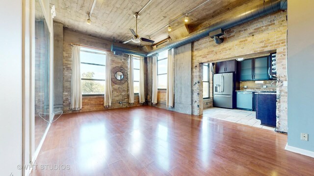 unfurnished living room featuring light hardwood / wood-style floors, brick wall, ceiling fan, and track lighting