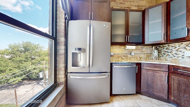 kitchen featuring a sink, appliances with stainless steel finishes, backsplash, light stone countertops, and glass insert cabinets