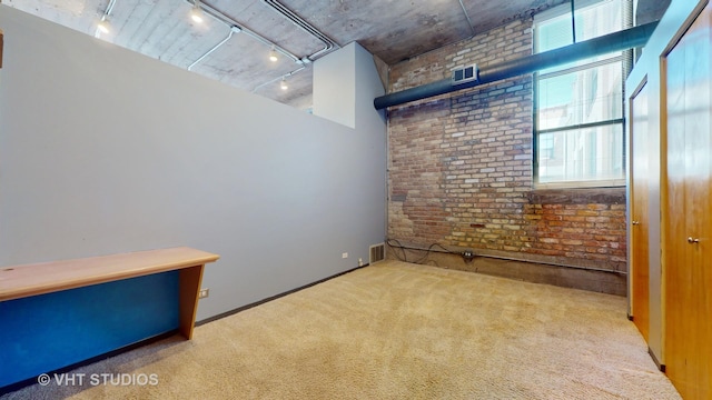 carpeted empty room featuring brick wall, visible vents, and track lighting