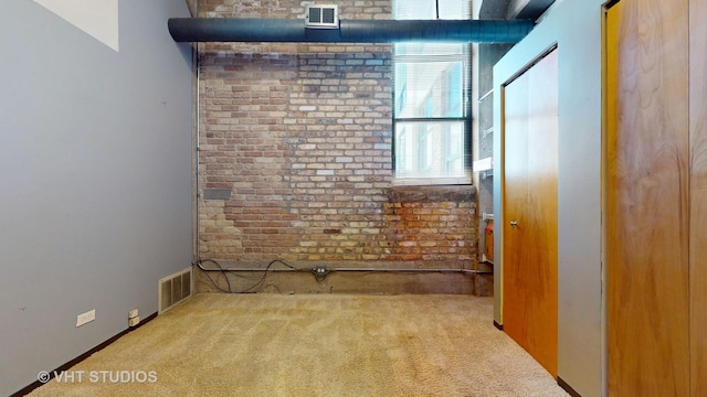 carpeted empty room with brick wall and visible vents