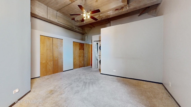 unfurnished bedroom featuring stacked washer and clothes dryer, multiple closets, light colored carpet, a towering ceiling, and ceiling fan