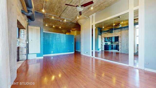 unfurnished living room featuring track lighting, a high ceiling, wood-type flooring, and ceiling fan