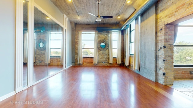 empty room with a ceiling fan, brick wall, and wood finished floors