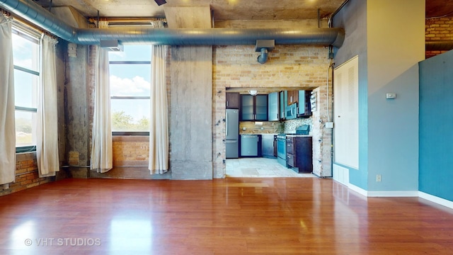 empty room with brick wall, wood finished floors, and baseboards