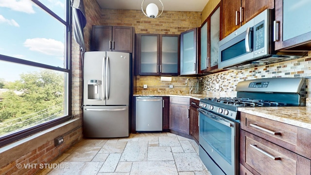 kitchen featuring light stone counters, glass insert cabinets, a sink, stainless steel appliances, and backsplash