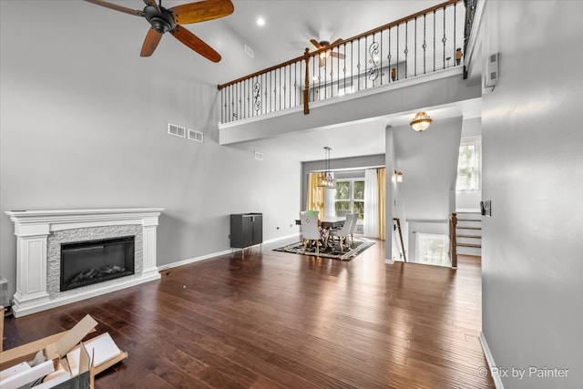 living room featuring a high ceiling, ceiling fan, a fireplace, and dark wood-type flooring