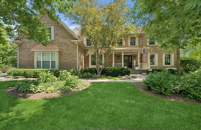 traditional-style home featuring a front yard, covered porch, and brick siding
