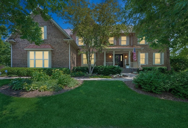 traditional home featuring a porch, a front yard, and brick siding